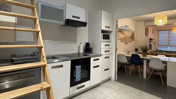 A modern kitchen with a skylight, a wooden ladder, and a dining area with a pool table.