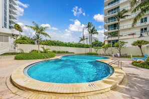 Zona de piscina con indicador de profundidad de 1.8 metros, rodeada de palmeras y un edificio de varios pisos.