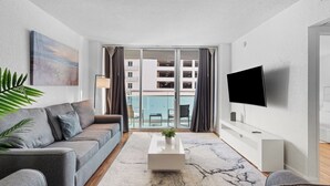 A modern living room with a grey sofa, a white coffee table, and a TV on the wall.