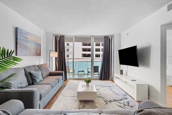 A modern living room with a grey sofa, a white coffee table, and a TV on the wall.