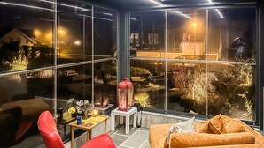 A modern room with a glass wall, a red chair, a yellow sofa, and a small table with a candle and a bottle.