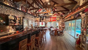 A bar area with wooden furniture, shelves with bottles, and a view through large windows.