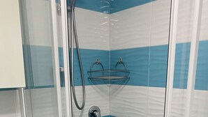 A bathroom with blue and white striped tiles, a glass shower enclosure, a white sink, and a glass shelf. - Ponzamania Siren (Le Forna)