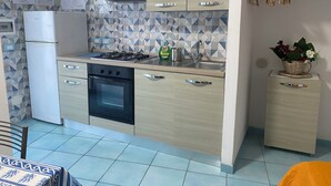 A modern kitchen with a refrigerator, stove, oven, and sink. There are cabinets and a tiled backsplash. - Ponzamania Siren (Le Forna)