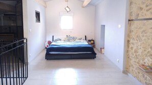 Ein Schlafzimmer mit Bett, Fenster, Treppe und einer Steinwand.