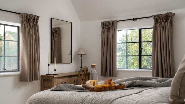 Une chambre à coucher avec un grand lit, une commode en bois, un miroir et une fenêtre avec des rideaux.