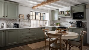 Une cuisine avec des meubles de couleur verte, un plan de travail en marbre, une table de salle à manger ronde avec des chaises, et une fenêtre donnant sur l’extérieur.