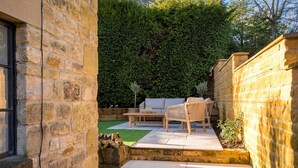 Un mur de pierres, un banc en bois, un canapé et une petite table dans un coin du jardin.