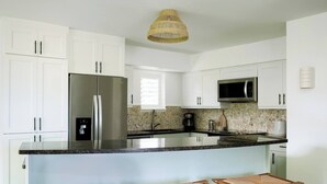 Une cuisine moderne avec des armoires blanches, des appareils en acier inoxydable, un grand îlot central doté de tabourets et un luminaire suspendu.