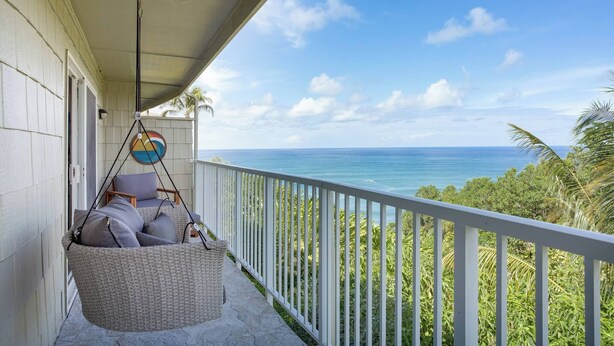 Un balcon avec un fauteuil suspendu, une balustrade blanche et une vue sur l’océan.