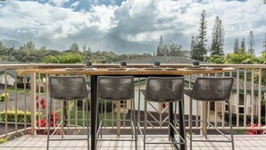 A balcony with a table and chairs, overlooking a mountainous landscape with a cloudy sky. - New Deluxe A/C Home, Spectacular Mountains Views (Princeville)