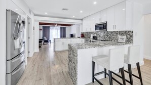 A modern kitchen with white cabinets, a marble island, stainless steel appliances, and a dining area with white chairs.
