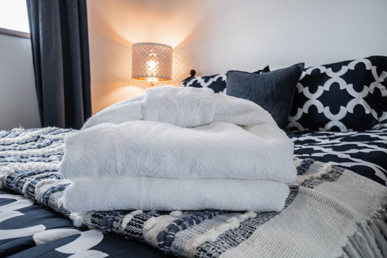 Un lit bien fait, recouvert d’un drap blanc et d’un plaid à motifs.