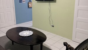 A room with a round table, a television mounted on the wall, and a patterned chair.