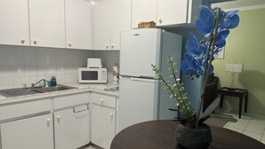 A kitchen with white cabinets, a microwave, a refrigerator, a sink, and a dining table with a potted plant.