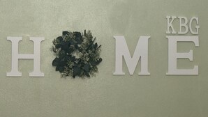 A wall with the words "HOME" and "KBG" in large letters, with a wreath in between.