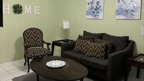 A living room with a sofa, armchair, coffee table, and artwork on the walls.