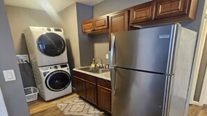 A compact kitchen with a stainless steel refrigerator, a built-in washer and dryer, wooden cabinets, and a small sink.