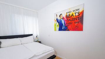 Een slaapkamer met een bed, een nachtkastje, een wanddecoratie en een raam met gordijnen.