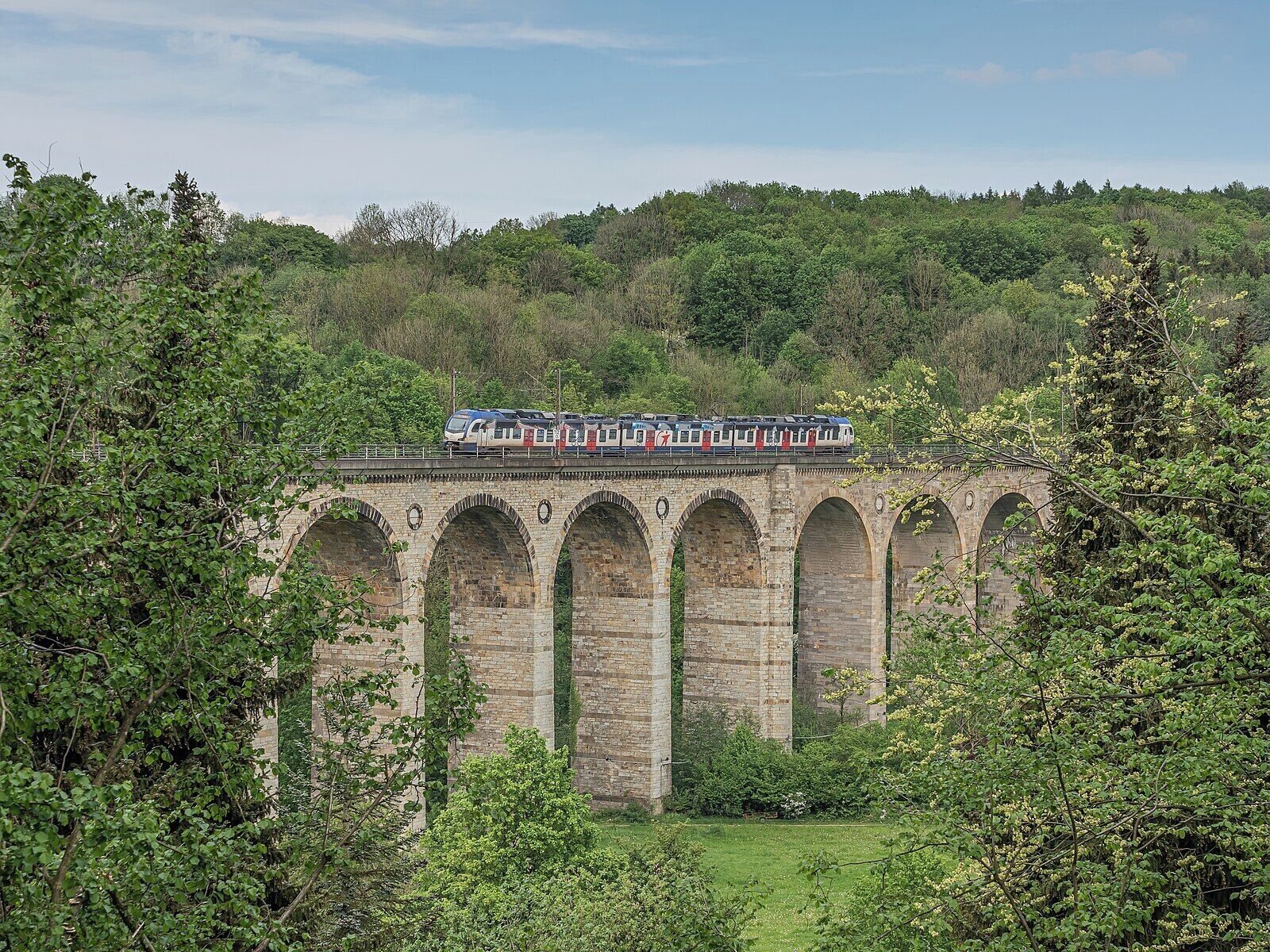 A train on a stone viaduct surrounded by greenery.