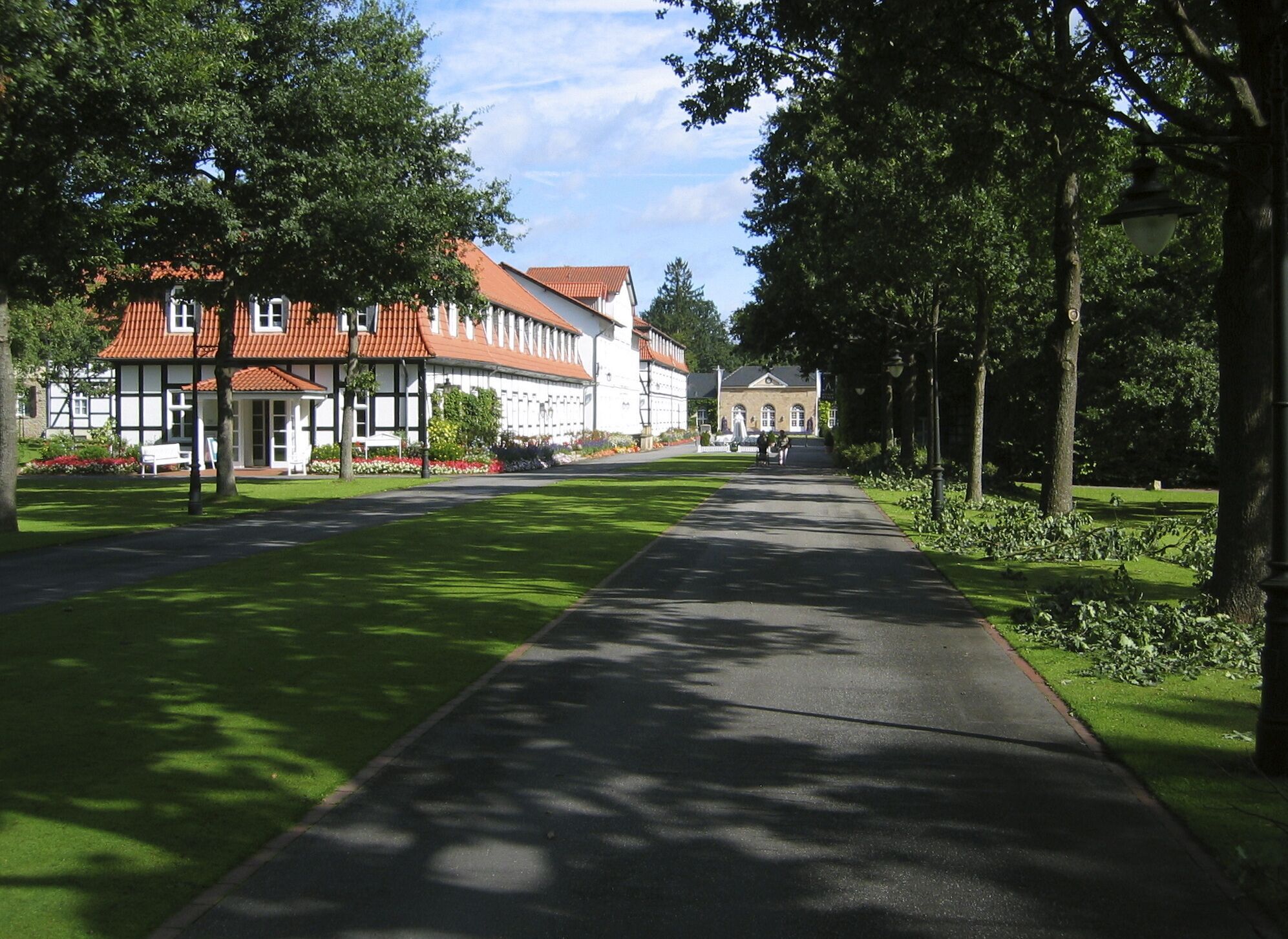 Ein Weg führt zu einem Gebäude mit roten Ziegeldächern, umgeben von Bäumen und einem gepflegten Rasen.
