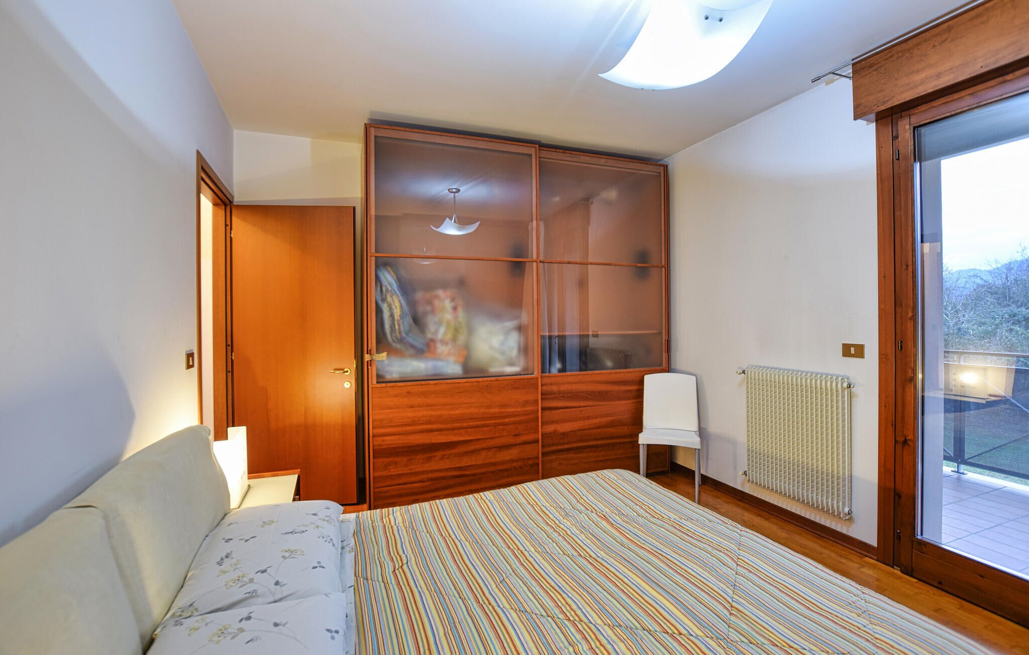 A bedroom with a bed, a wardrobe, a radiator, and a large window.