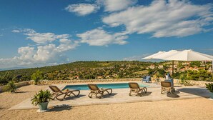 A poolside area with lounge chairs and a large umbrella, overlooking a hillside with buildings. - Cozy home in Bobovisca (Bobovisca)