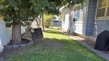 A residential backyard with a lawn, a tree, and a house with a white fence.