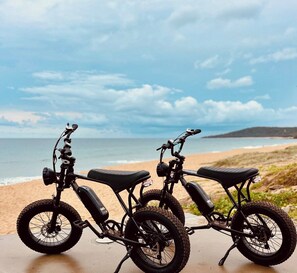 Two electric scooters parked on a concrete surface with a beach and ocean in the background.