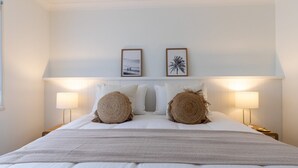 A neatly made bed with two pillows, a woven headboard, and two framed pictures on the wall. - Agnes Break | 3BR · Sauna & Walk to Beach (Agnes Water)
