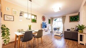 Ein modernes Wohnzimmer mit Essbereich, Holzboden und einem großen Fenster mit Vorhängen.