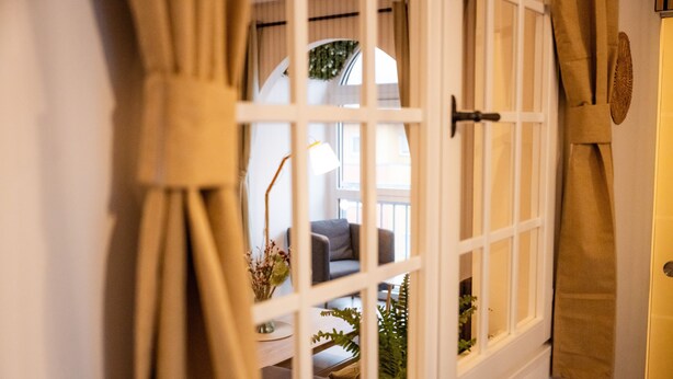 Ein Zimmer mit großem Fenster, Vorhängen, einer Couch, einer Lampe und einer Pflanze.