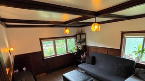 Un salon chaleureux avec un canapé foncé, un canapé de couleur claire et une table basse en bois. De grandes fenêtres laissent entrer la lumière naturelle et offrent une vue sur la verdure environnante.