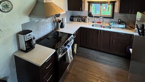 Une cuisine avec des meubles de rangement en bois, une cuisinière, un évier et une fenêtre donnant sur les arbres.