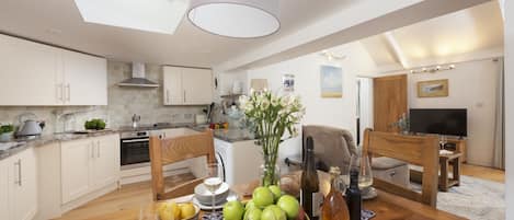 A modern kitchen with white cabinets, a dining area with a wooden table, and a living room with a TV and seating.