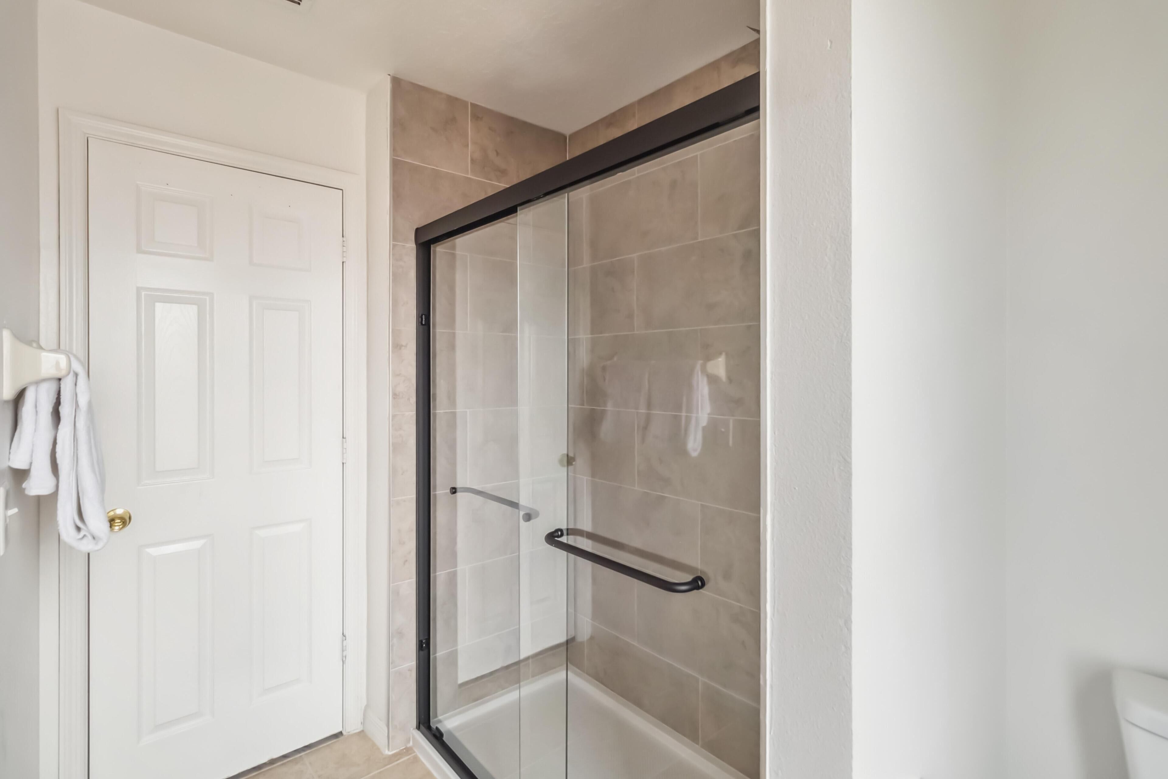 A bathroom with a glass shower enclosure, a white door, and a towel rack.