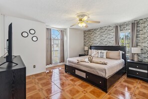 Une chambre avec un lit, un ventilateur de plafond, une télévision et un mur décoré d’un motif en briques.