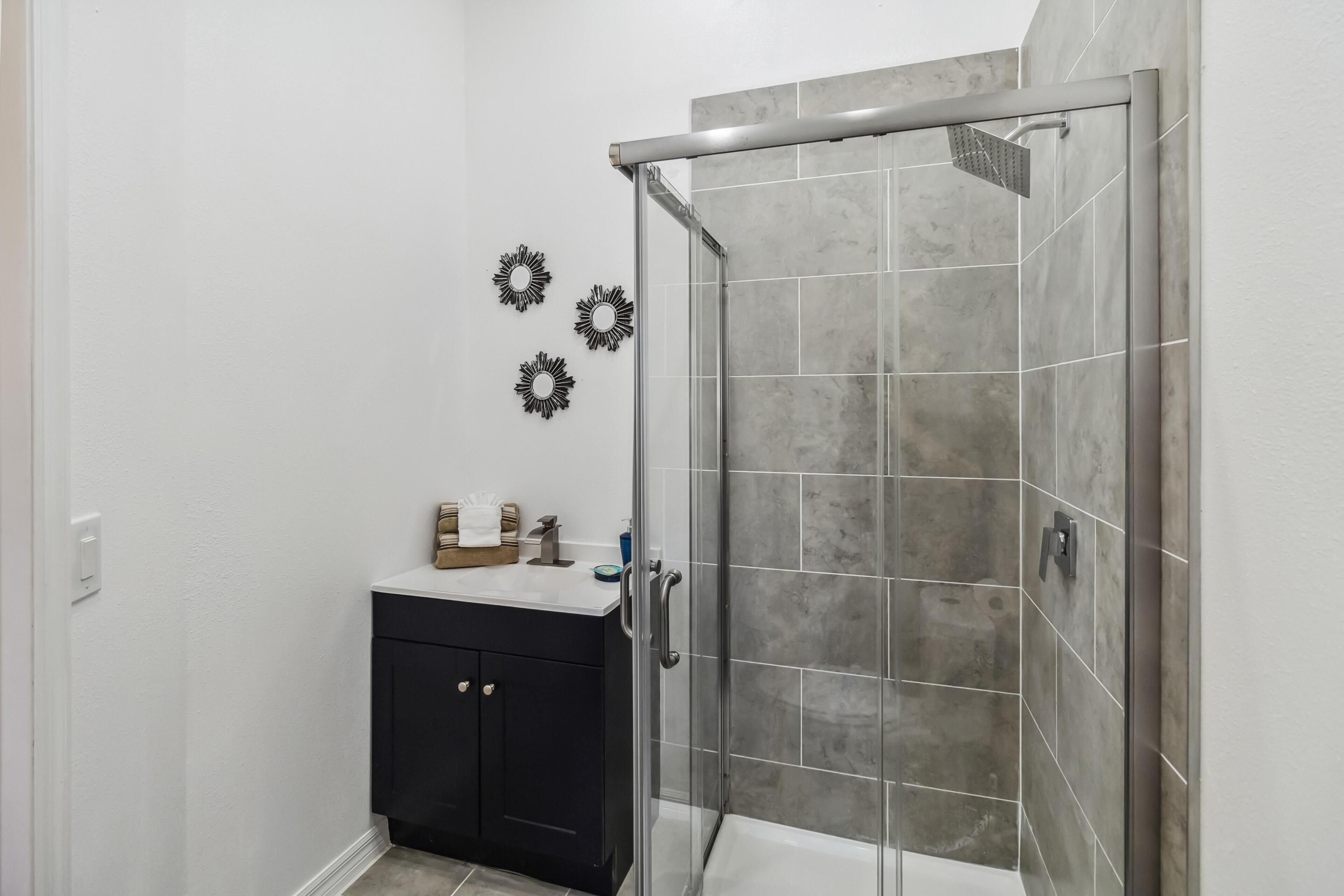 Ein Badezimmer mit einer Glaskabine zur Dusche, einem dunklen Schrank und dekorativen Wandbildern.