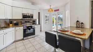 Une cuisine moderne avec des armoires blanches, des appareils en acier inoxydable et un comptoir en granit. On y trouve un coin repas avec des chaises noires et une petite table.