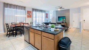 Une cuisine moderne dotée d’un îlot central, d’un coin repas avec des chaises et d’un téléviseur fixé au mur.