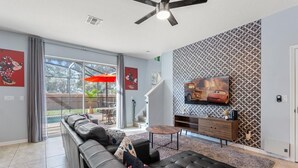 Un salon moderne avec un canapé en cuir, une table basse, un téléviseur fixé au mur et un escalier menant à l’étage supérieur.