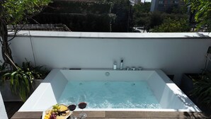 Un jacuzzi sur le toit, avec une terrasse en bois, entouré de verdure et avec les bâtiments de la ville en arrière-plan.