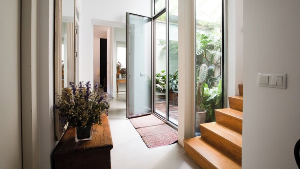 Un intérieur moderne avec un banc en bois, une plante en pot et une porte vitrée donnant sur un balcon agrémenté de plantes.