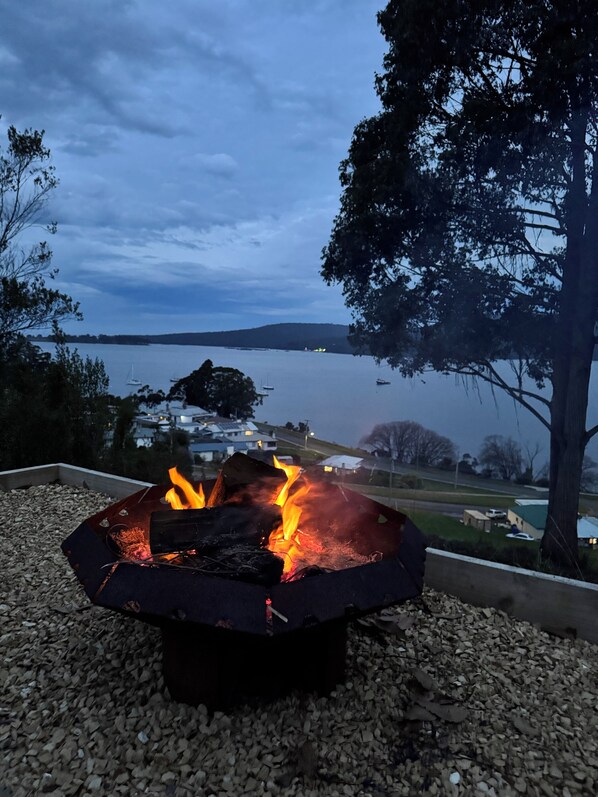 A fire pit with a view of a lake and distant buildings.