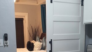 Une chambre à coucher comprenant un lit, une table de chevet, une chaise et une porte coulissante donnant sur une salle de bain.