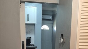 Une chambre à coucher comprenant un lit, une table de chevet, une commode et une porte donnant sur un coin cuisine.