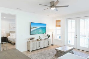 A spacious living room with a large flat-screen TV mounted on the wall, a ceiling fan, a dining area with a table and chairs, and a large window with a view of the ocean. - Enclave at Lyndell Lane by Avantstay Private Pool (Panama City Beach)