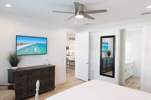 A bedroom with a bed, a ceiling fan, a TV, a dresser, and a view of the kitchen. - Enclave at Lyndell Lane by Avantstay Private Pool (Panama City Beach)