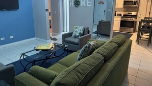 Olohuoneessa on vihreä sohva, sohvapöytä ja seinälle asennettu televisio.