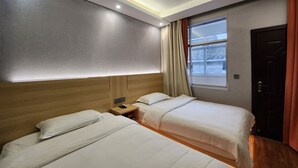A hotel room with two beds, a wooden headboard, a nightstand, and a window with curtains. - Biancheng International Youth Hostel (Xiangxi)